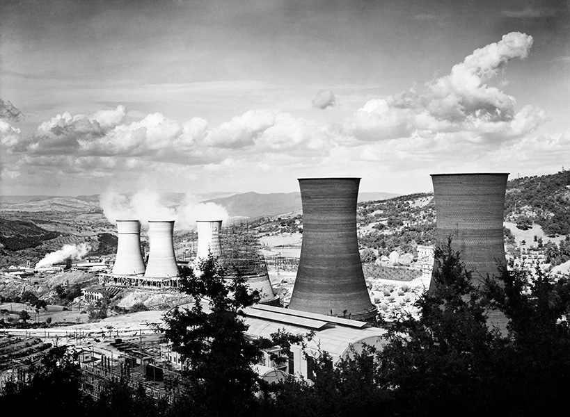 Black and white photo of bucolic landscape studded with large industrial cooling towers.