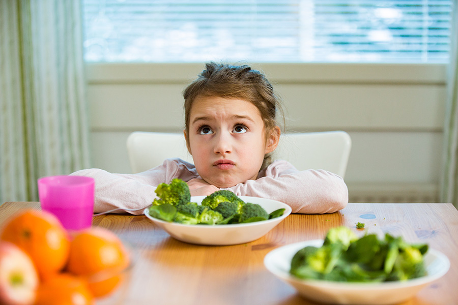 An unhappy little girl confronts a dish of broccoli.