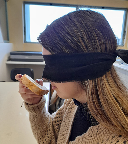 A blindfolded woman smells a piece of bread.
