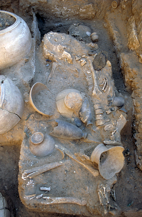 Squelette d'une femme dans une tombe sur le site de l'ancienne ville d'Oum el-Marra, dans l'actuelle Syrie. Un bébé gît près de son genou gauche, caché par des récipients en poterie sur cette photo. Un pendentif en or a été trouvé à son cou — un signe qu'elle avait un statut élevé.