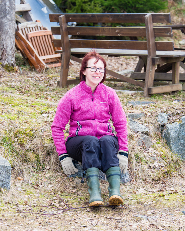 Photograph of Sara Riggare sitting on the ground wearing pink jacket and green Wellington boots. She is smiling.