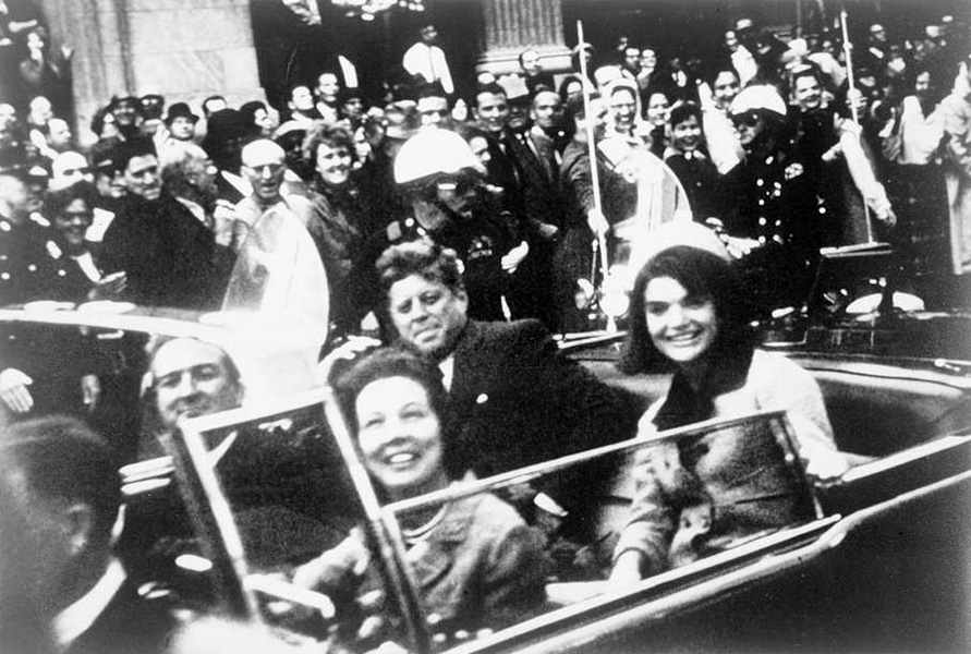 A grainy, black and white photograph taken November 22, 1963 shows President John F. Kennedy in a car with his wife Jackie Kennedy, along with Texas Governor John Connally and his wife, Nellie. They are smiling and a crowd is cheering.