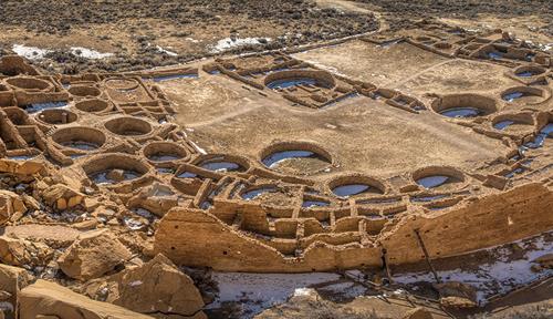 Aerial view of Pueblo Bonito, in Chaco Canyon, New Mexico. The site has a semicircular shape with clusters of rectangular rooms . Pueblo Bonito has more than 600 rooms arranged on multistory levels. These rooms enclose a central plaza.