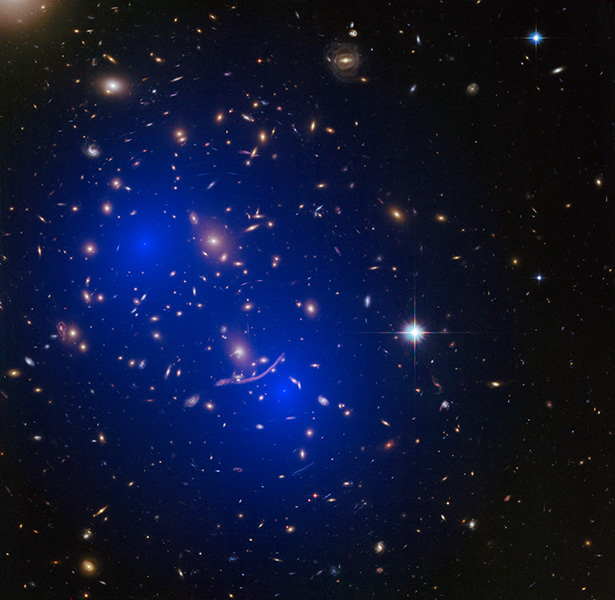 Image from the Hubble Space Telescope shows an array of galaxies. Two areas of blue shading show where scientists mapped concentrations of invisible mass within the cluster thought to be dark matter.