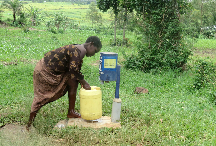 A young woman places a large, yellow jug under a chlorine dispenser.