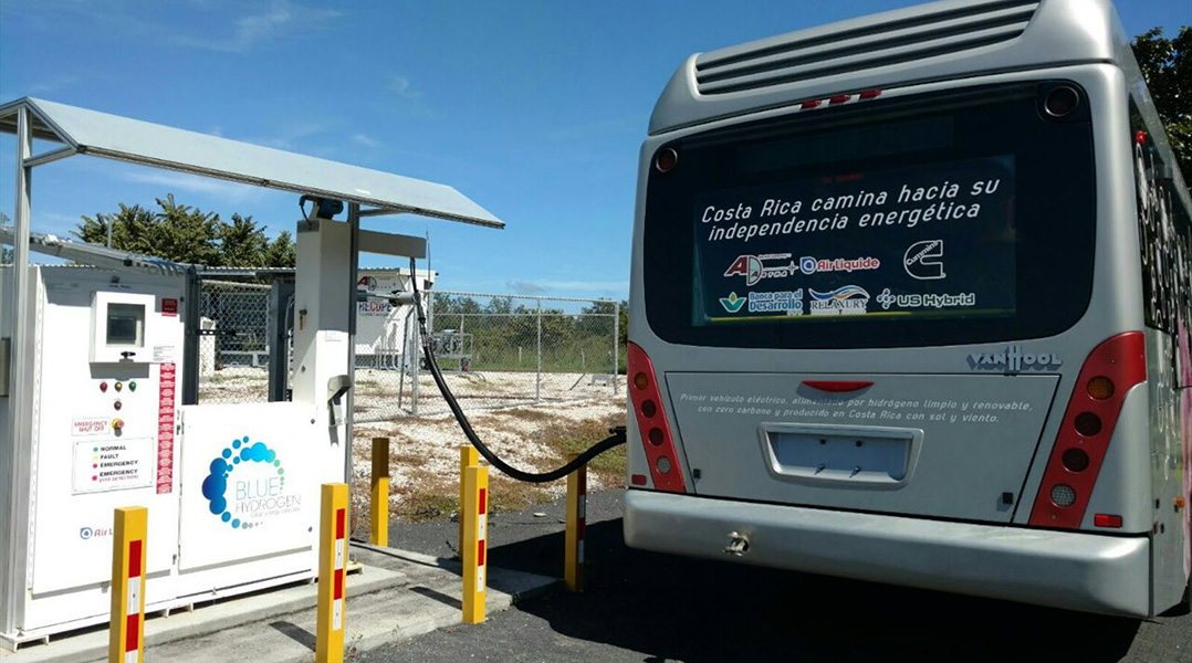 Photo shows a gray hydrogen fuel cell electric bus being loaded with fuel. On the back of the bus reads the legend “Costa Rica walks toward its energy independence.”