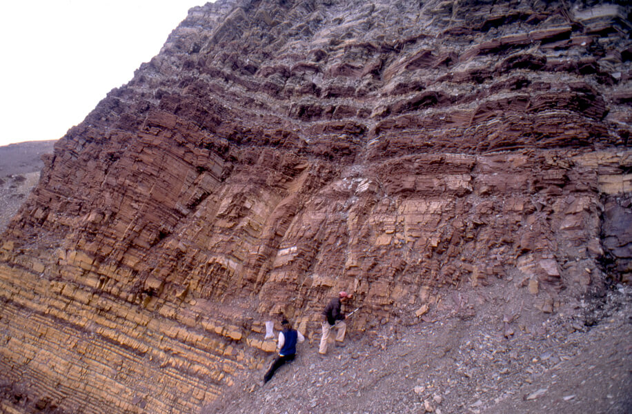 Photograph of a 2002 field expedition Paul Hoffman took to northeastern Svalbard, Norway. Geoscientists Galen Halverson and Matthew Hurtgen are seen collecting carbonate rocks from a mountainside. The carbonate rocks rest directly above glacial deposits from the second Snowball Earth event. This juxtaposition of carbonates — which form only in warm parts of the ocean — and glacial rocks supports the theory that ice covered the entire planet during the Snowball Earth episodes.