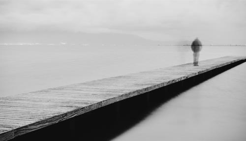 Photograph of a man walking on a wooden jetty at the water, under cloudy skies. Despair-induced suicidal thoughts and actual attempts are recognized as distinct things by researchers, who are working to better understand the progression and so intervene more effectively.