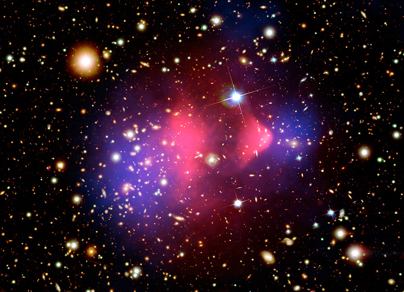 Composite image shows galaxy cluster 1E 0657-556 through multiple wavelengths. Hot gas, shown in pink, has been detected with the Chandra X-ray telescope. Magellan and Hubble provided the optical images of the colliding galaxies. The bulk of the matter in the collision is dark matter, shown in blue and calculated by analyzing the effect of gravitational lensing.