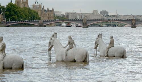 Photo of the Rising Tide sculpture by artist Jason deCaires Taylor installed within the tidal range on the Thames River in 2015; the sculpture was composed of four large, cement-gray horses with riders, the river’s high tide submerges the horses’ flanks.