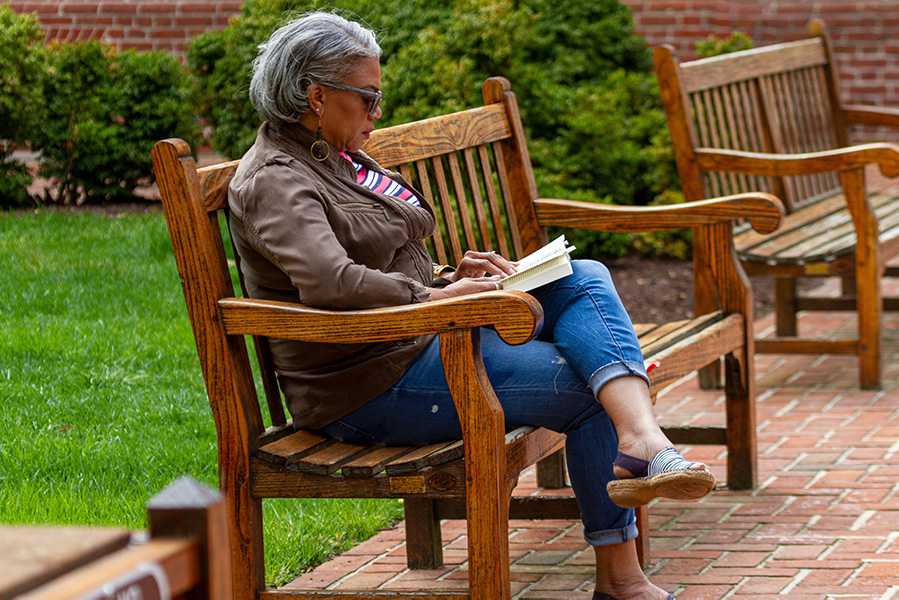 Photograph of an elderly woman sitting on a park bench reading a book.