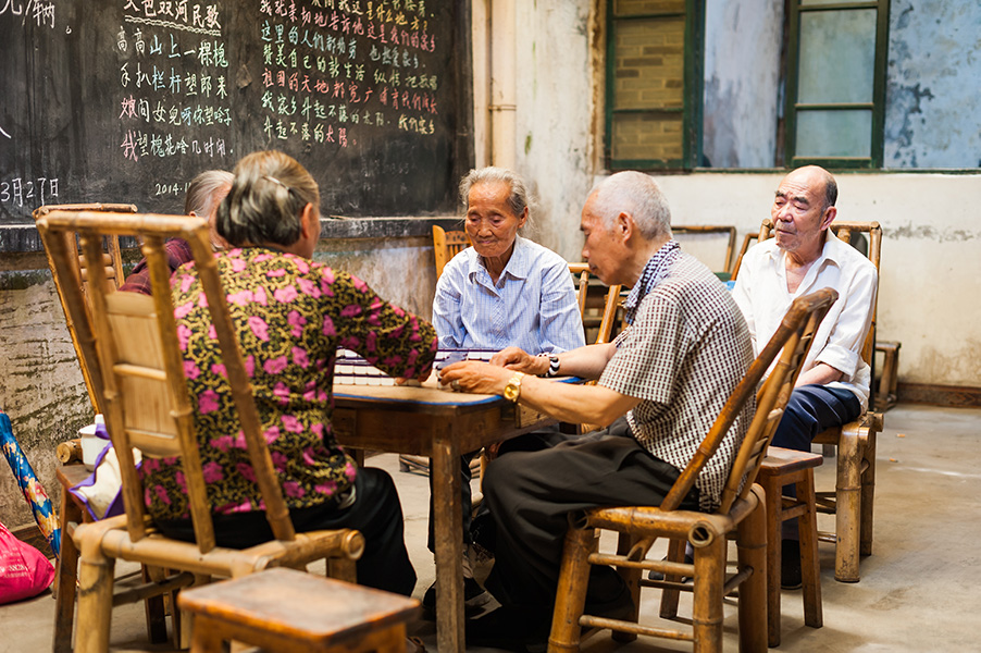 Photograph of five elderly people sitting around a table playing mahjong.