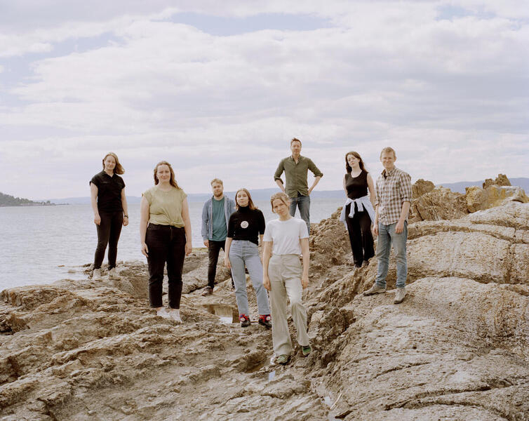 Photograph of eight young people standing on a rocky shoreland.