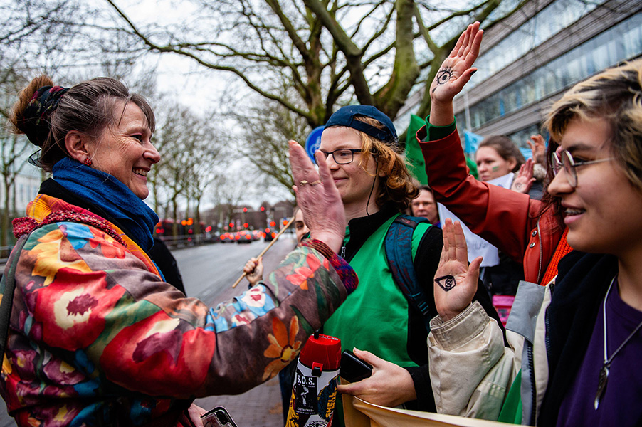Photo of a woman in a colorful jacket beaming and raising her palm up to meet that of another woman. Others stand by smiling.