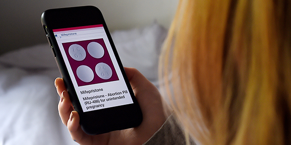 Photo illustration of someone looking at information about mifepristone, used to terminate early pregnancies, on their smartphone.