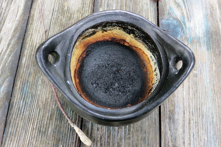 Photo shows a round pot with a layer of blackened, burnt food on the bottom. 