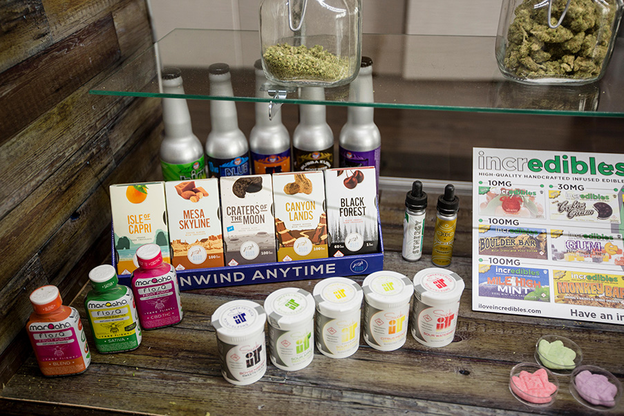 Photograph of a range of cannabis edibles, including chocolate bars, bottles of candies, drinks and tinctures on display at a dispensary. 