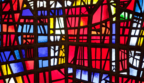 Photograph shows light shining through a colorful stained glass window of the church at Skalholt in Iceland.