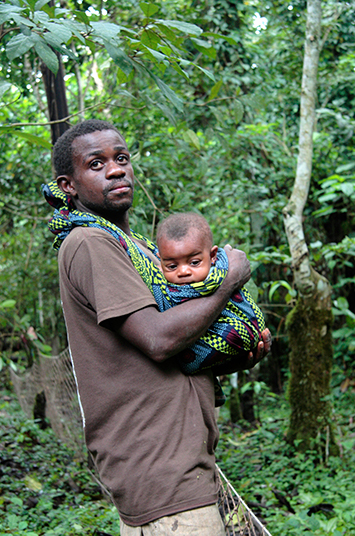 A Congolese man carries his infant child in a carrier on his chest while hunting in the forest.