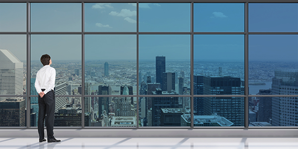 Photo of a man looking out on a city through a large set of windows tinted from dark to clear