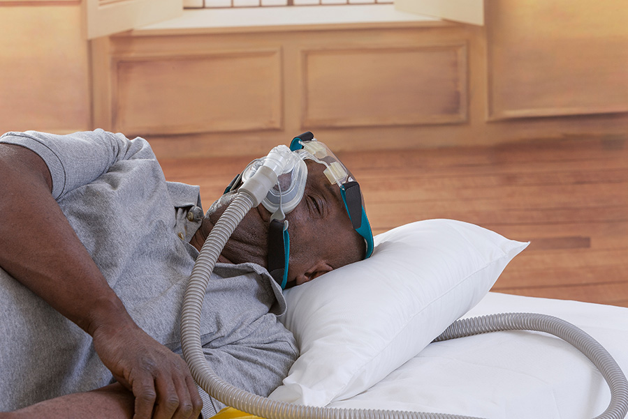 A Black man with sleep apnea using a CPAP machine to help him breathe as he sleeps.