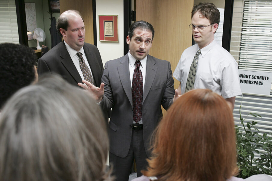A still from the US version of the TV series The Office showing underlings gathered round incompetent boss Michael Scott.