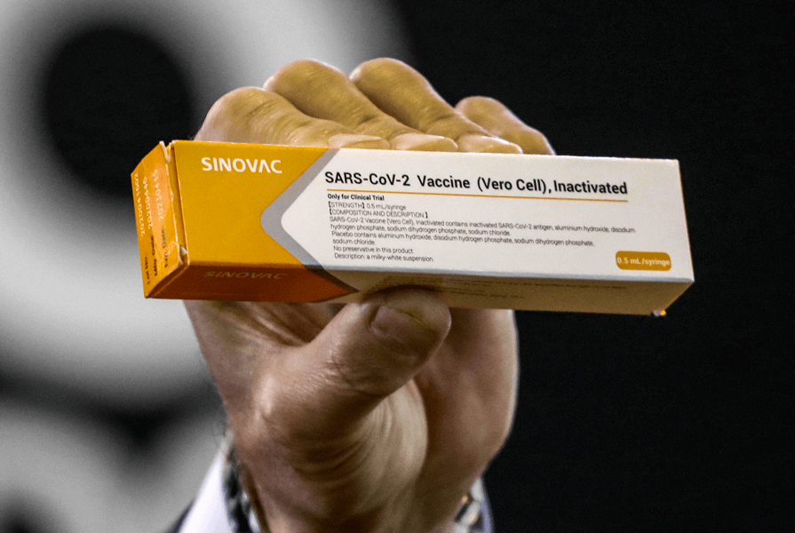 Photograph of a hand holding a small yellow, grey and white box with the words “Sinovac,” “SARS-CoV-2 Vaccine” and “Inactivated” printed on it.