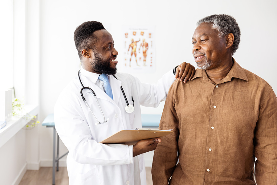 Photo of an elderly Black man talking with a younger Black doctor