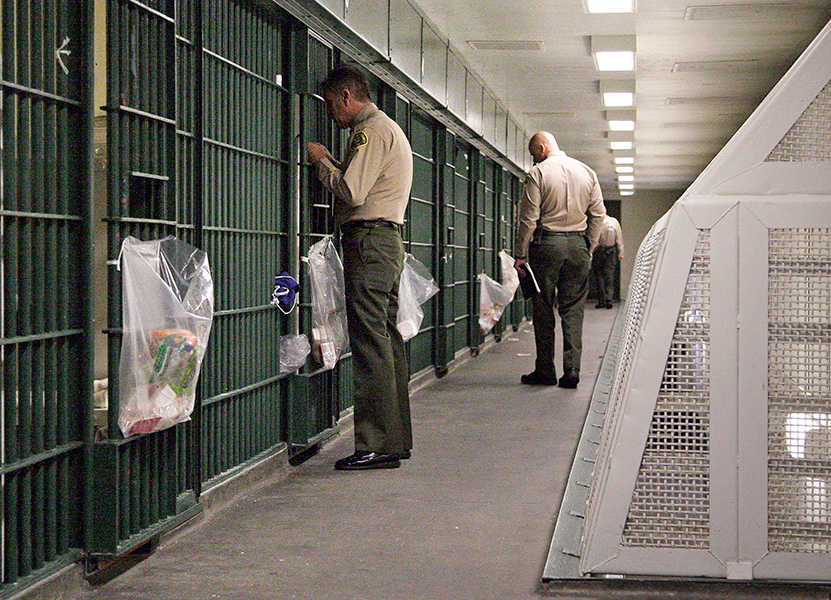 Uniformed officers inspect a cell block in a jail.