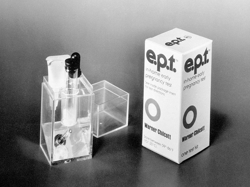 Photo shows an advertisement for a home pregnancy test from the 1970s; the test consists of a plastic container with a test tube and other vials of chemicals necessary to run the test.