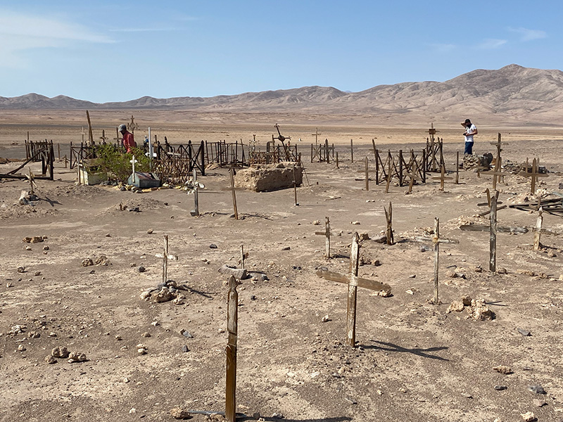 A stark small graveyard with plain wooden crosses and some old fencing sits in the desert