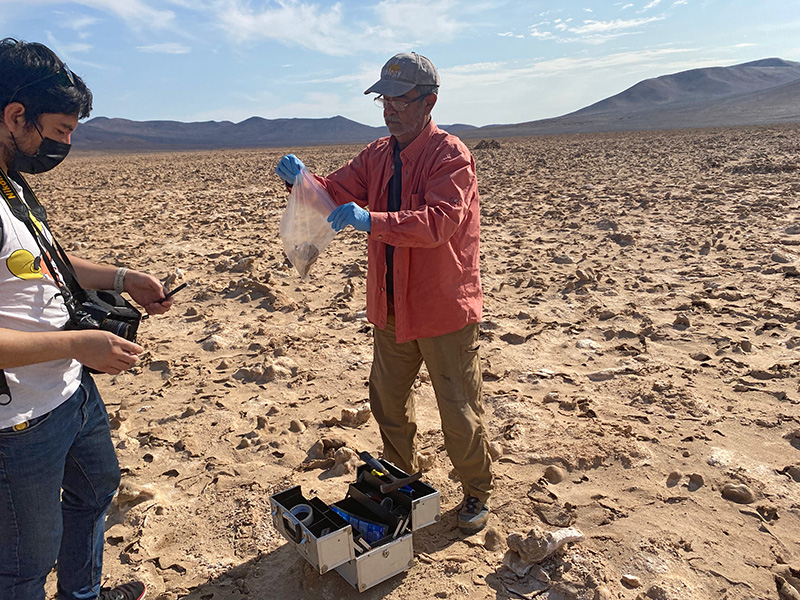 Two researchers collect samples of rock under the baking sun.