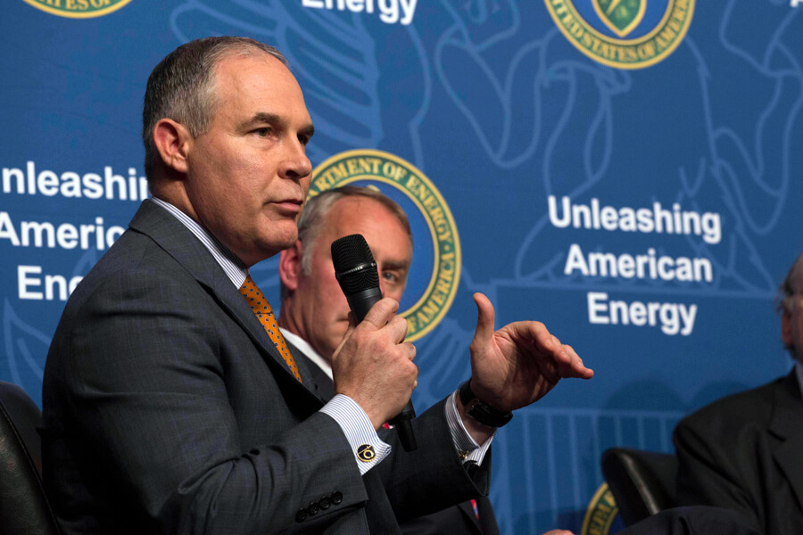 Photograph of Scott Pruitt speaking into a microphone. Behind him is a backdrop printed with the US Department of Energy logo and the phrase “Unleashing American Energy.”