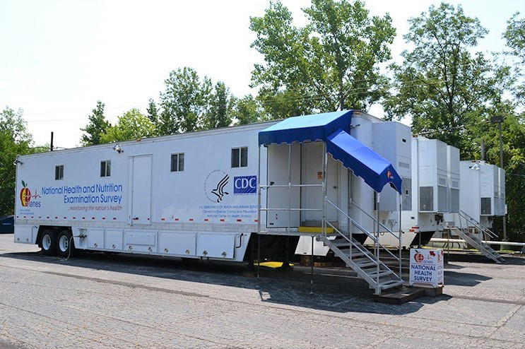 Photo shows three large trailers installed in a parking lot with NHANES and CDC logos.
