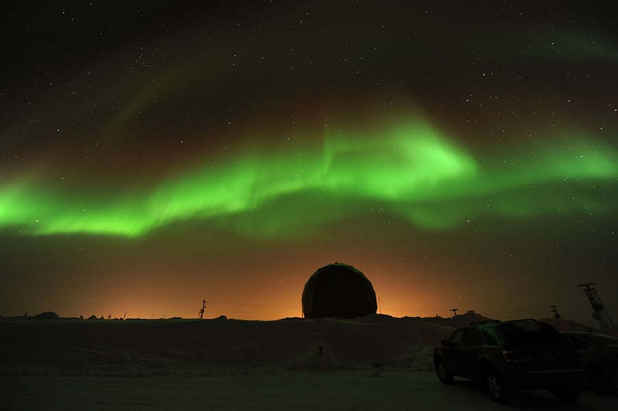 Image shows the green glow of the northern lights hovering above a nighttime landscape.