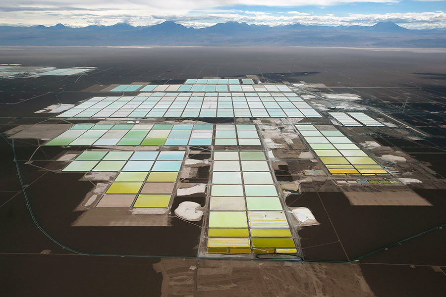 A desert landscape photographed from high up shows a mining plant with many rectangular pools of different shades of blue, green and yellow.
