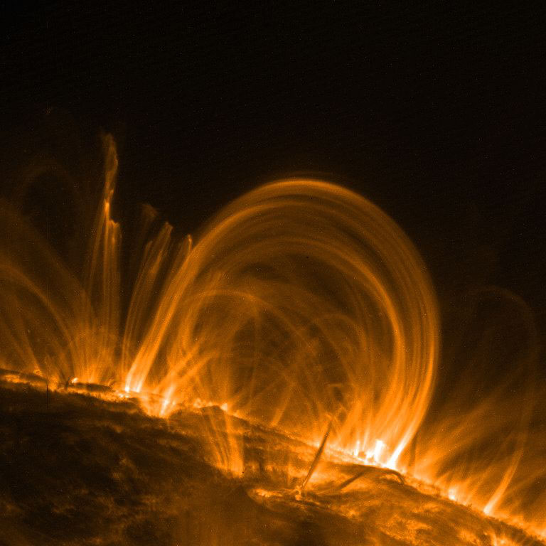 UV image shows a close-up of a cluster of glowing coronal loops traveling in an arc over the sun’s surface.