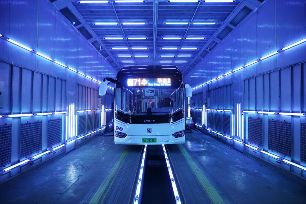 Photograph of an empty bus in a tunnel surrounded by lamps that are glowing violet.