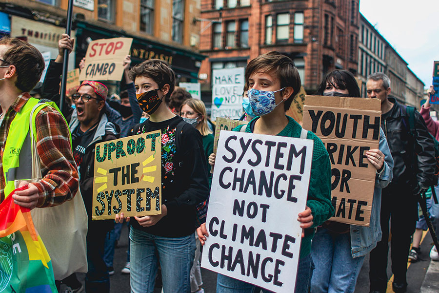 In a news photo on September 24, 2021 in Glasgow, Scotland, youths carry homemade signs as part of a street march demanding climate action. Signs bear messages such as: “System Change Not Climate Change”; “Uproot the System”; “Stop Cambo”; and “Make Love Not Emissions.”