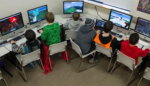 Photo shows a class of students sitting in front of monitors playing a game.