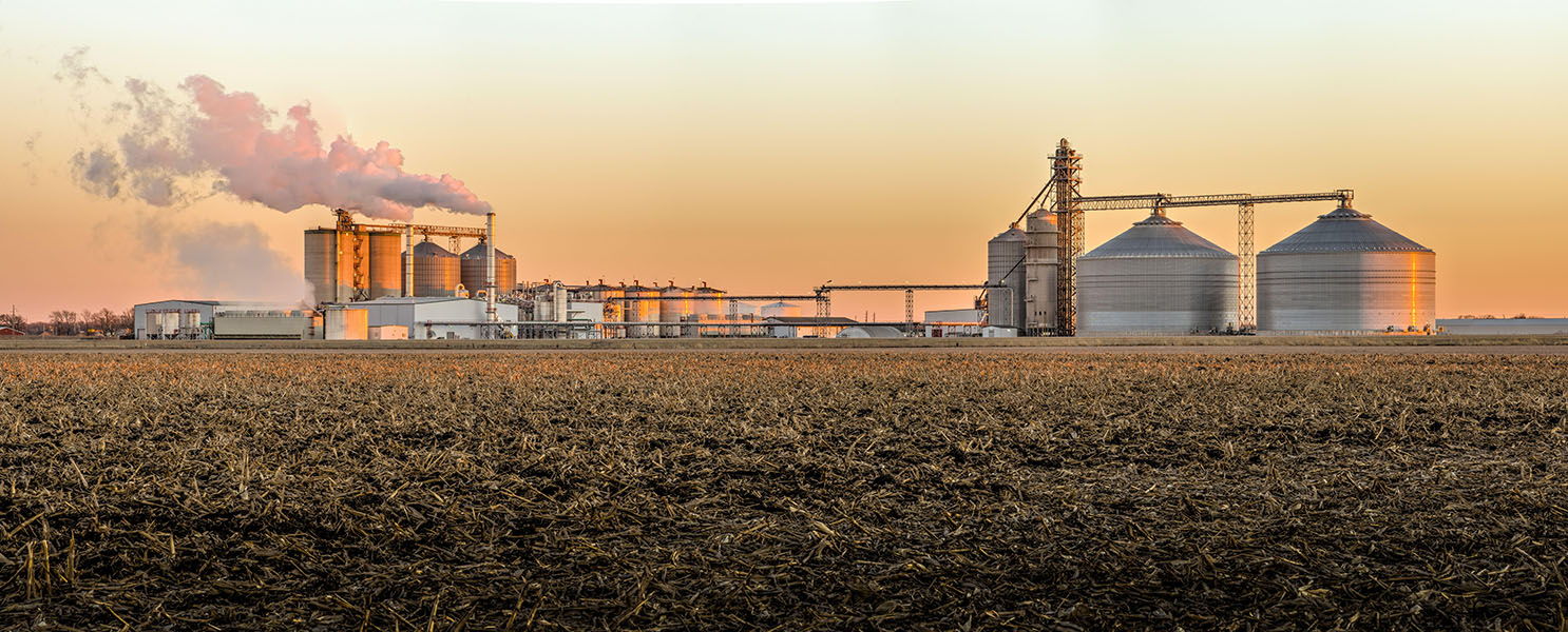Photograph of an ethanol plant, with large containers and other structures that have fumes coming out of them.