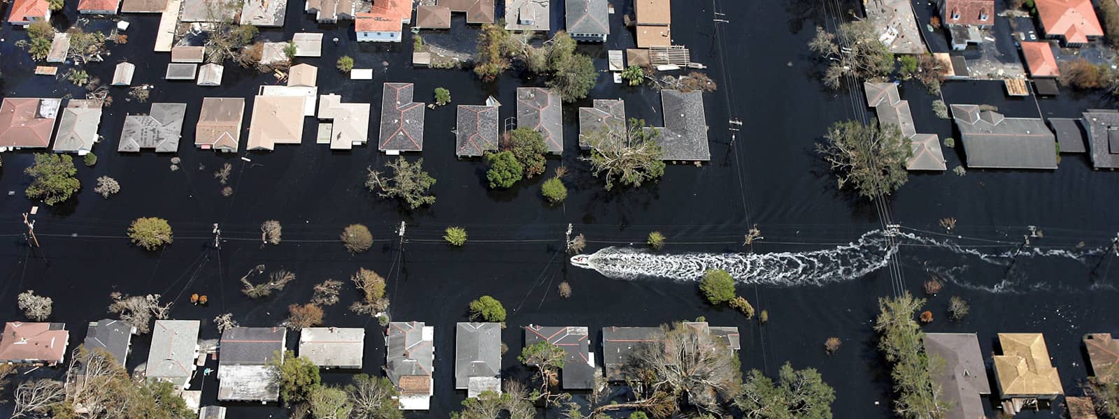 A small boat leaves a wake among houses surrounded by floodwaters.