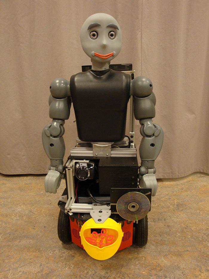 A humanoid robot on wheels wields a CD player and bubble blower.