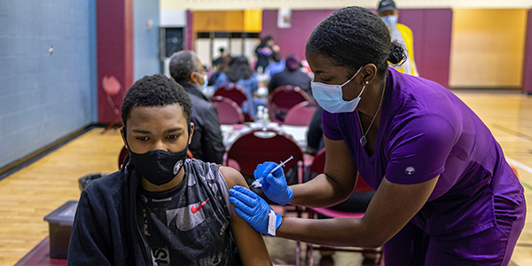 A teenager in a mask receives a vaccine from a medical provider