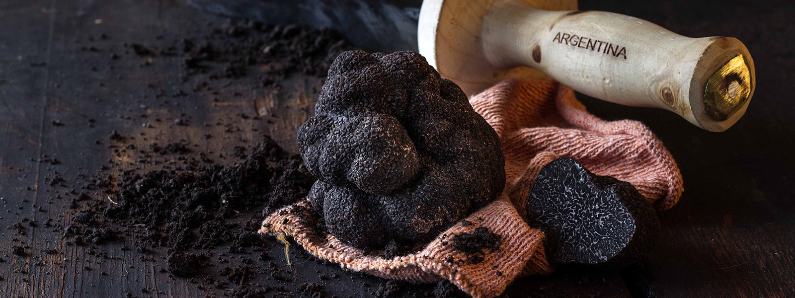 On a dark wooden board, a black truffle rests on an orange cloth and, in the background, a knife with the word 'Argentina' written on its wooden handle.