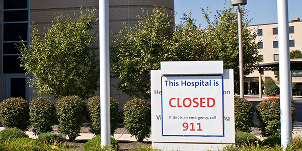 Photo shows the exterior of a large building with a sign saying “This Hospital is CLOSED. If this is an emergency, call 911.”