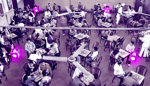 Una foto aérea teñida muestra a un grupo de personas sentadas en las mesas de una cafetería con lámparas que emiten luz violeta.