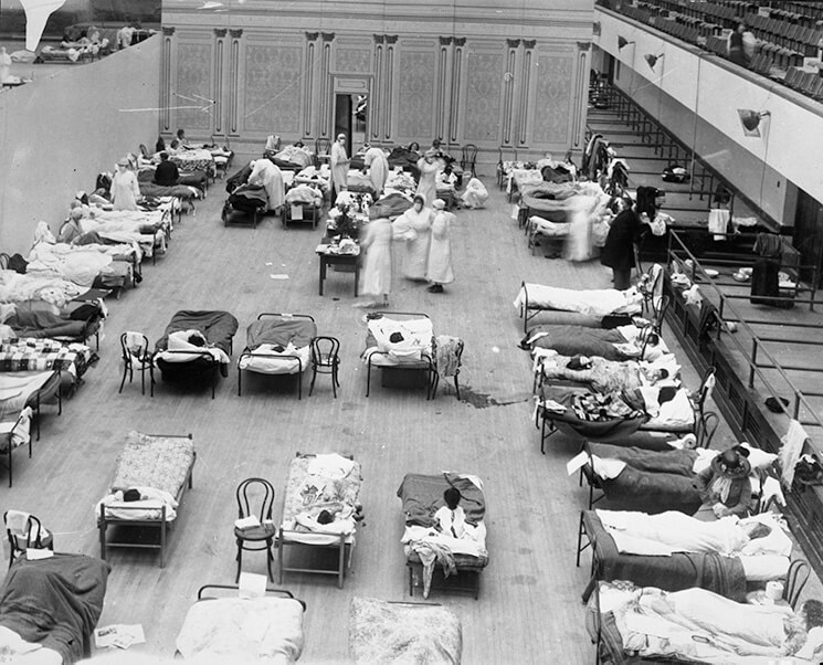 Black-and-white photo depicts volunteer nurses from the American Red Cross tending influenza sufferers in the Oakland Auditorium, Oakland, California, during the influenza pandemic of 1918.