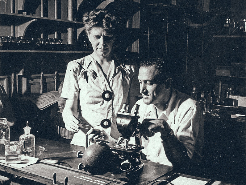 Photo from 1945 shows malaria researchers Seward Miller, seated at a microscope and Aimee Wilcox, standing, in the Atlanta lab that became the CDC.
