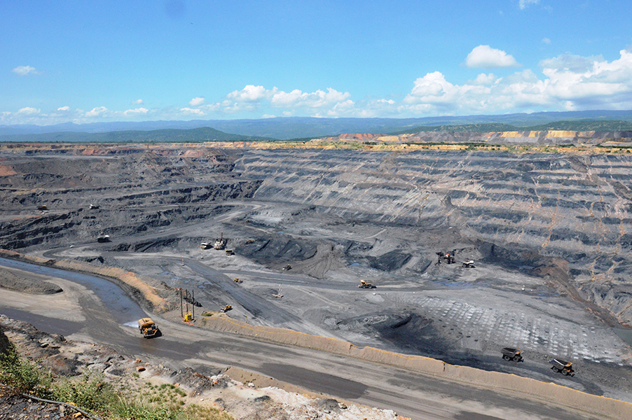 Panoramic view of the open pit coal mine El Cerrejón. Under a clear blue sky, grey circular roads and several tractors can be seen on these tracks. 